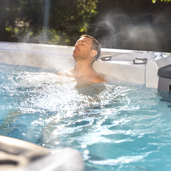 A man relaxing in the water with steam coming off of the water's surface.