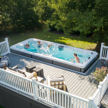 Family playing in a swim spa that is surrounded by a deck.
