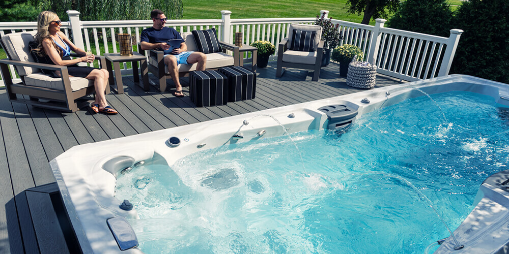 A couple relaxing around a swim spa controlling it with an app.