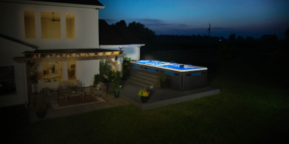 Night time shot of a swim spa in a backyard.