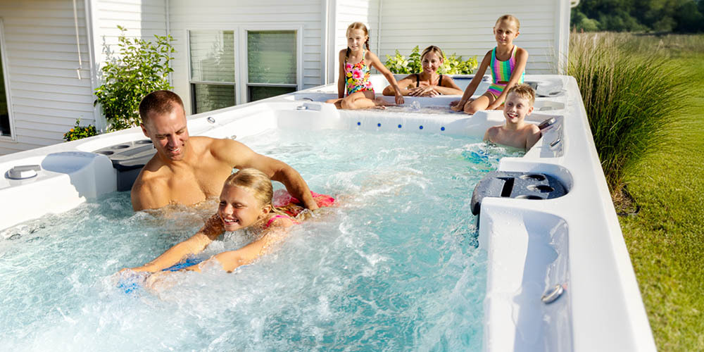 Family having fun in a swim spa and a girl using a kickboard to swim against the current.